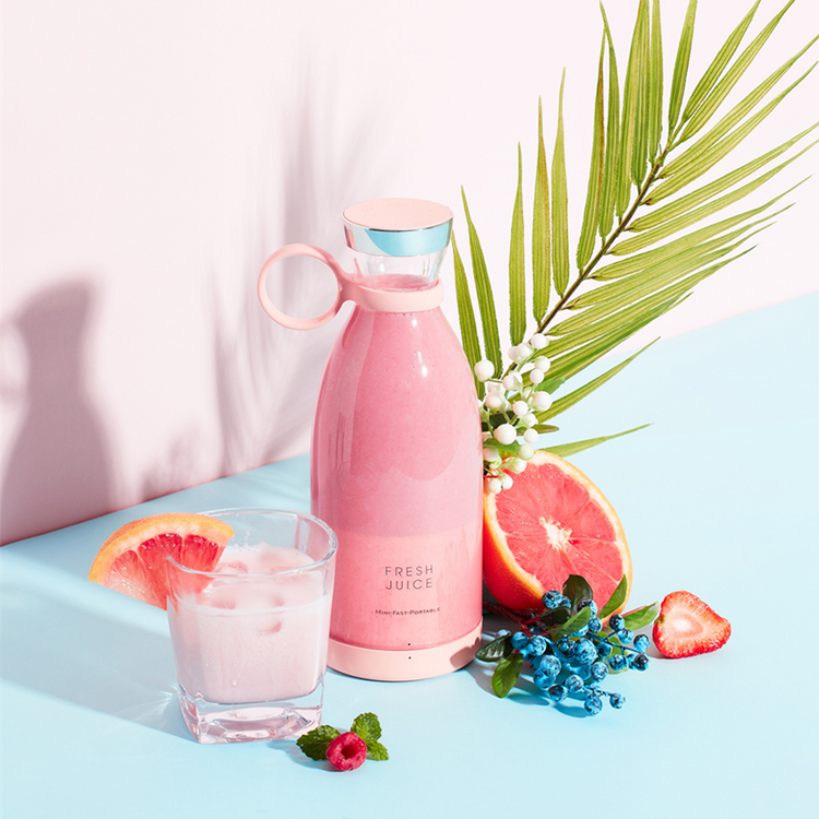 Pink portable blender filled with a strawberry smoothie, next to fresh grapefruit and berries